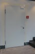 Eine graue Tür mit einem silbernen Türgriff und einem roten Feuermelder an der Wand daneben.