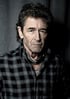 Porträt von Peter Maffay mit dunklem, lockigem Haar, kariertem Hemd und Halstuch vor einem grauen Vorhang.
