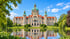 Das Neue Rathaus in Hannover mit grüner Kuppel spiegelt sich im Maschparkteich unter blauem Himmel.