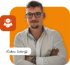 Lukas Scharff, junger Mann mit Brille und Bart, verschränkte Arme, Hemd, vor orangem Hintergrund.
