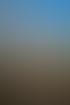 Frau kniet auf Schotterweg, wirbelt bunten Farbpulverstaub in die Luft, blauer Himmel mit Wolken im Hintergrund.