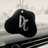 Schwarzer Autolufterfrischer mit weißem „Dc“-Logo hängt vor einem Armaturenbrett.