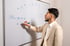 Mann im Anzug schreibt mit blauem Marker auf ein Whiteboard mit Diagrammen und "240k".