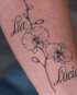 Filigranes Fineline-Tattoo einer Orchidee mit Blüten und Knospen sowie den Namen Lia und Lucia in Schreibschrift auf der Haut.
