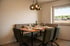 Modernes Esszimmer mit Holztisch, Eckbank, zwei Stühlen und Hängelampen, gedeckt für vier Personen.