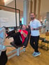 Ein Mann trainiert an einer Beinpresse im Fitnessstudio, während ein Trainer daneben steht; beide zeigen den Daumen nach oben.