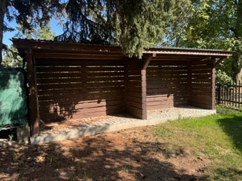 Offener Holzunterstand im Garten unter Bäumen