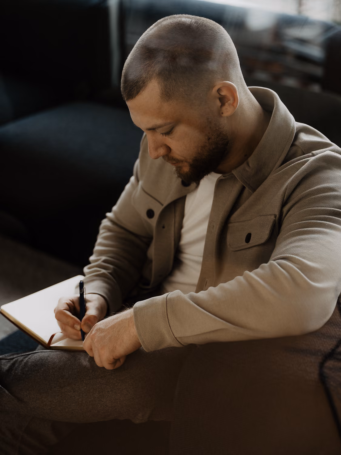 Ein Mann mit kurzem Haar und Bart schreibt konzentriert mit einem Stift in ein Notizbuch.