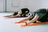 Zwei Frauen in Sportkleidung üben Yoga in der Kinderhaltung auf orangefarbenen und violetten Matten.