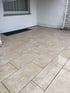 Beigefarbene Terrassenplatten aus Naturstein in rechteckigem Format mit dunklen Fugen vor einer weißen Hauswand.