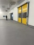 Ein Mann steht in einem großen, leeren Raum mit grauer Bodenfläche, weißen Wänden und zwei gelben Rolltoren.