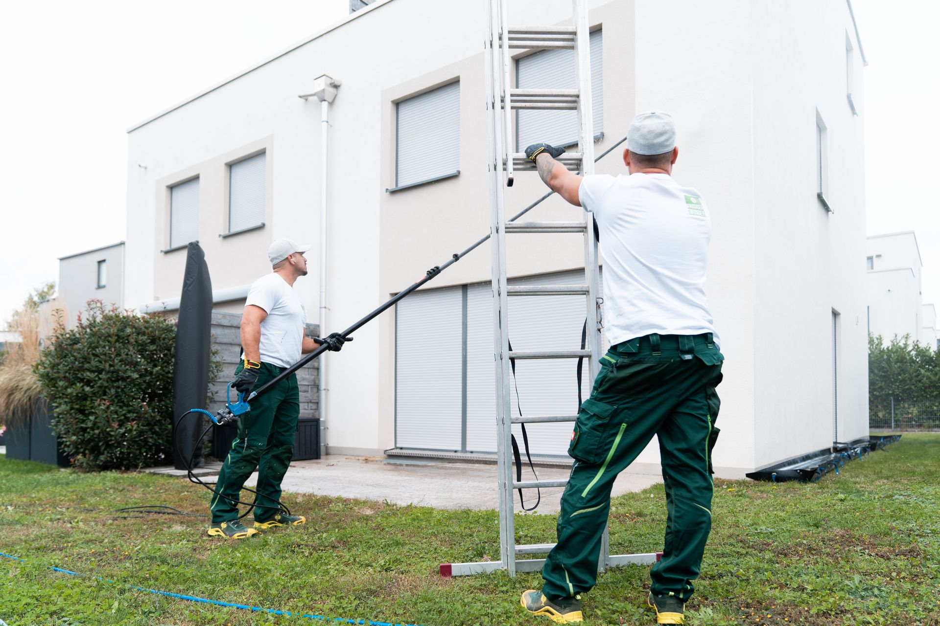 Zwei Mitarbeiter reinigen eine Fassade mit der Teleskoplanze vom Boden aus