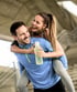 Smiling couple in activewear, one giving the other a piggyback.