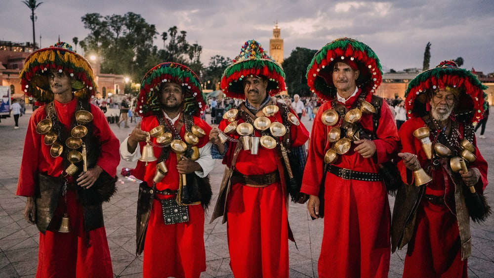 Fünf Wasserträger in roter Tracht mit Messingschalen auf dem Platz in Marrakesch