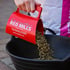 Hand schüttet Pferdefutterpellets aus einem roten Connelly's Red Mills Messbecher in einen schwarzen Eimer.