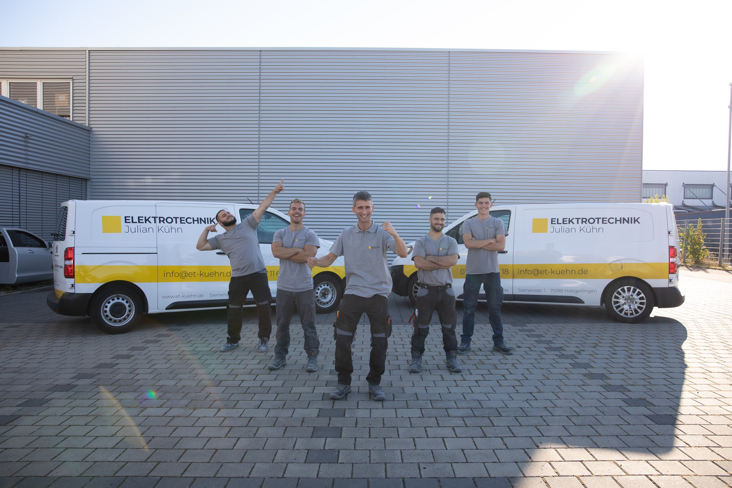 Fünf Monteure von Elektrotechnik Kühn stehen vor ihren Firmenfahrzeugen.