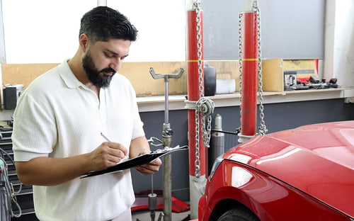 KFZ-Gutachter Sobeir Esmaty notiert die Schadenaufnahme an einem Fahrzeug in der Werkstatt