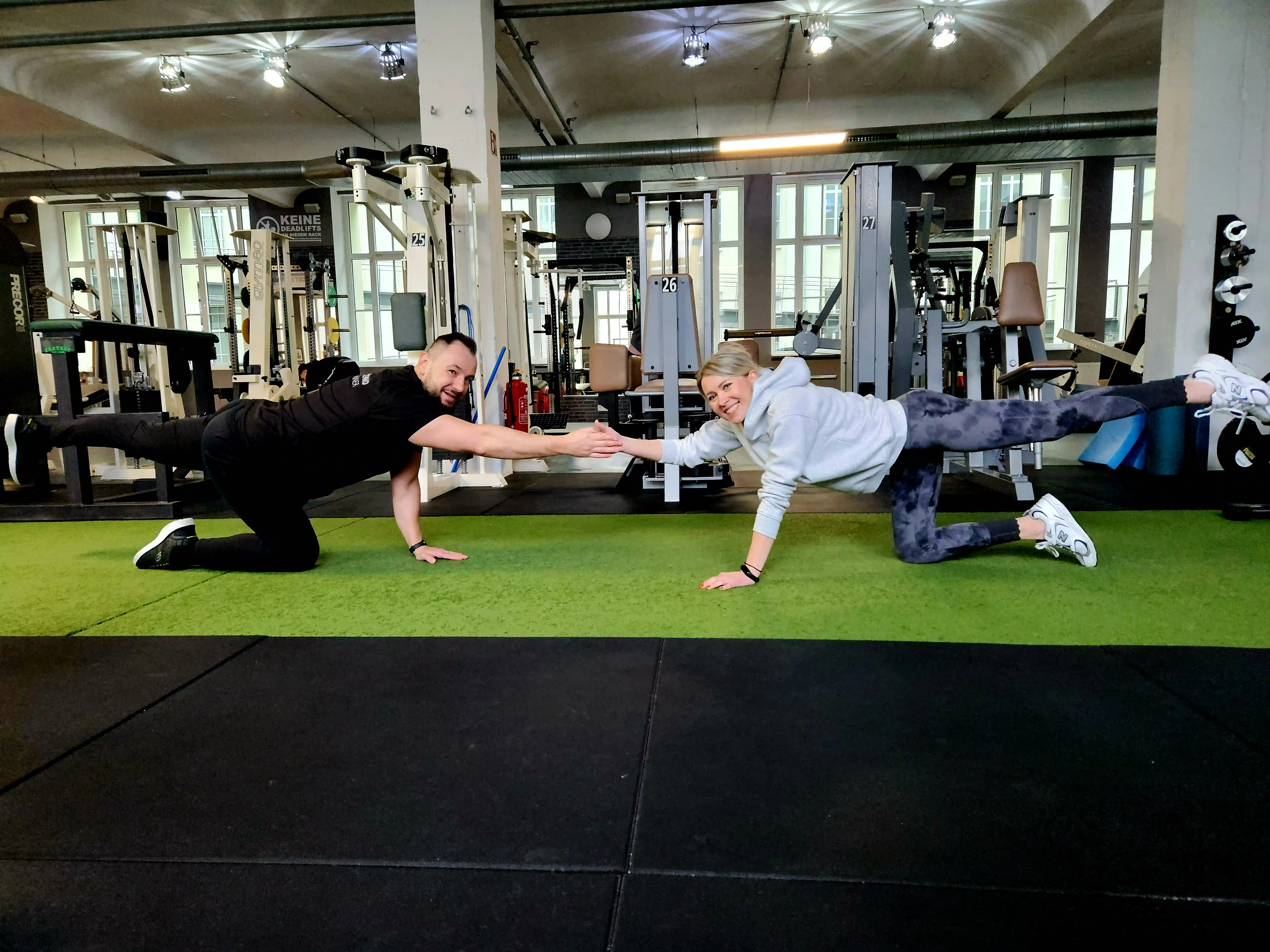 Zwei Sportler im Fitnessstudio, die auf allen Vieren den Arm und das gegenüberliegende Bein ausstrecken.
