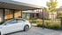Weißes Elektroauto lädt unter einem Carport vor einem modernen Haus mit Garten.