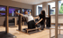 Ein Mann trainiert mit Kurzhanteln an einem Holz-Rückentrainer, während eine Trainerin ihn im Fitnessstudio anleitet.