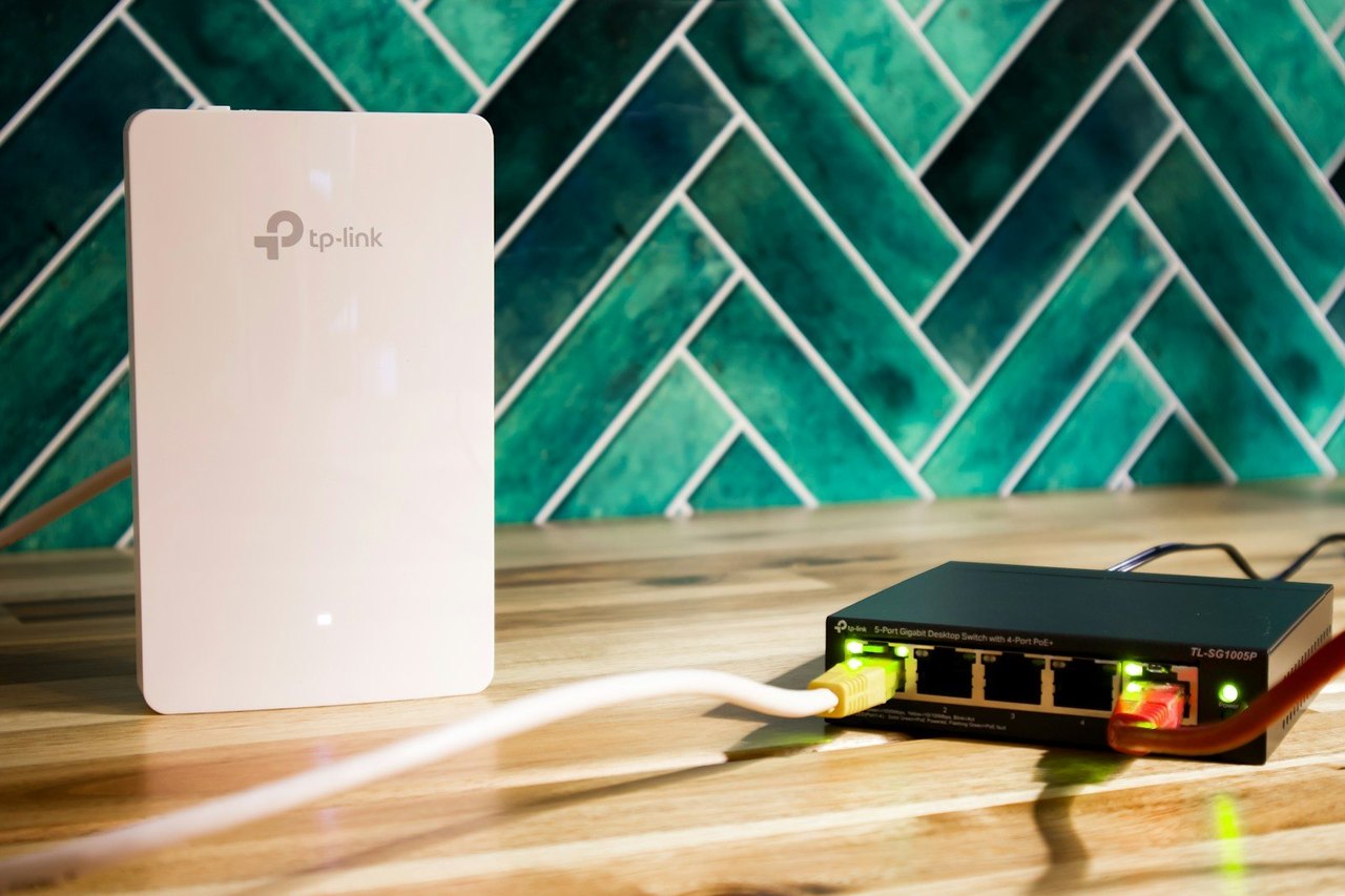 Weißer WLAN-Access-Point und ein kleiner Netzwerk-Switch mit Kabeln auf einem Holztisch