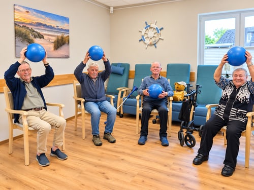 Vier Menschen machen im Sitzen Übungen mit blauen Bällen.