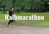 Mann in schwarzer Sportkleidung läuft auf einem Waldweg mit Text "Halbmarathon".