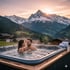 Ein Paar entspannt sich in einem Whirlpool im Freien mit schneebedeckten Bergen und Sonnenuntergang im Hintergrund.