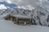 Eine rustikale Holzhütte mit schneebedecktem Dach, umgeben von tiefem Schnee und schneebedeckten Bergen.