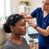 A technician in blue scrubs adjusts EEG electrodes on a woman's head during a neurological brain activity scan.