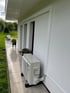 Eine Wärmepumpe steht auf einer Terrasse vor einer weißen Hauswand.
