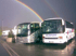 Zwei Reisebusse parken unter einem Regenbogen auf nassem Asphalt.