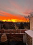 Leere Terrakotta-Blumentöpfe auf einem Balkon vor einem leuchtend orange-roten Abendhimmel über einer Wohnsiedlung.