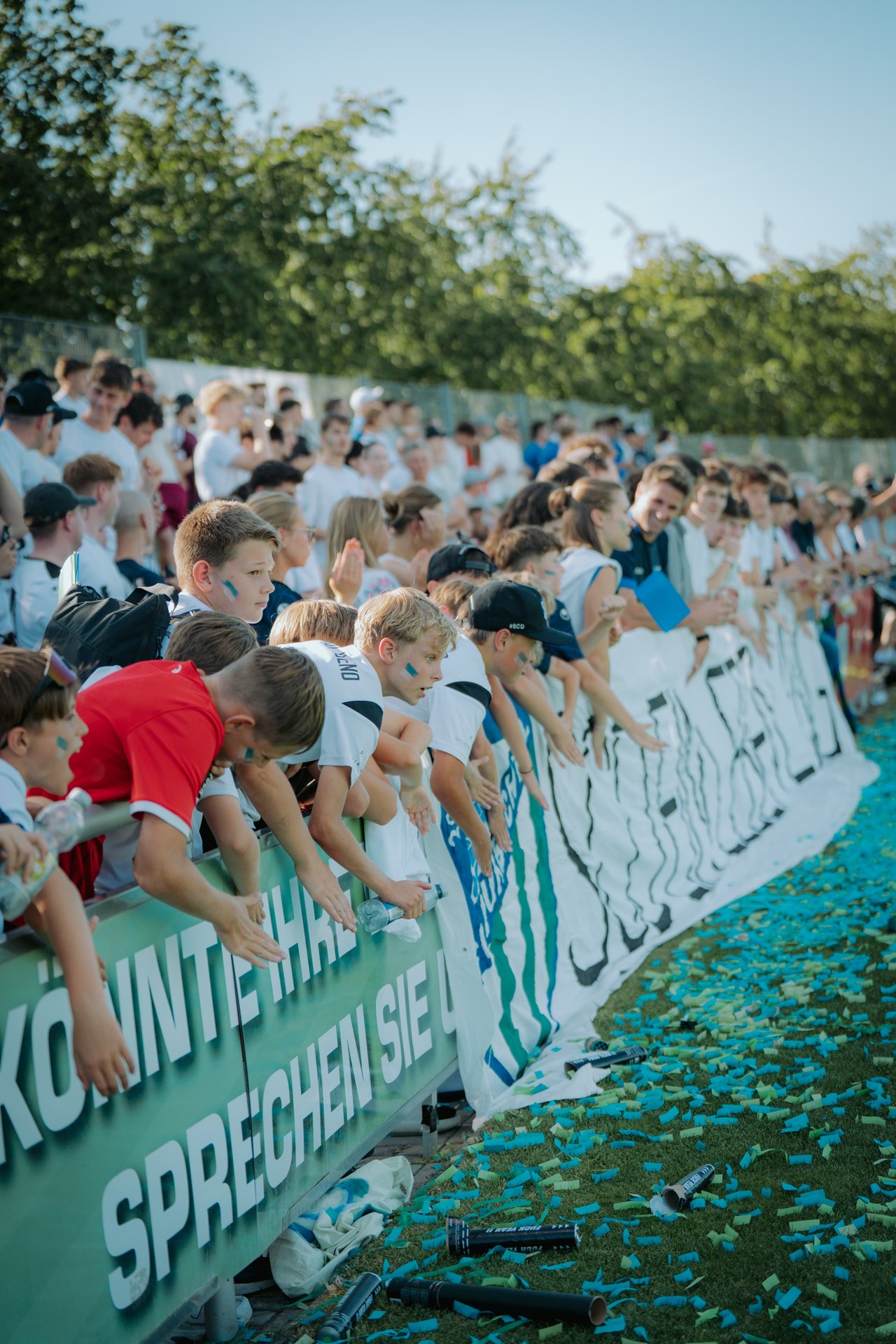Fans beugen sich ueber die Bande, Konfetti auf dem Rasen