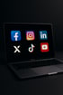 Ein offenes MacBook Pro zeigt auf dem Bildschirm sechs Social-Media-Logos: Facebook, Instagram, LinkedIn, X, TikTok, YouTube.