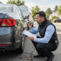 Ein Gutachter untersucht den Schaden an der Stoßstange eines grauen Autos und macht sich Notizen.