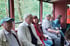 Fünf Personen sitzen in einem offenen Zugabteil vor grüner Landschaft.
