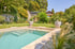 Moderner Swimmingpool mit Treppeneinstieg in einem grünen Garten mit Rasenfläche, großen Pflanzkübeln und Bäumen.