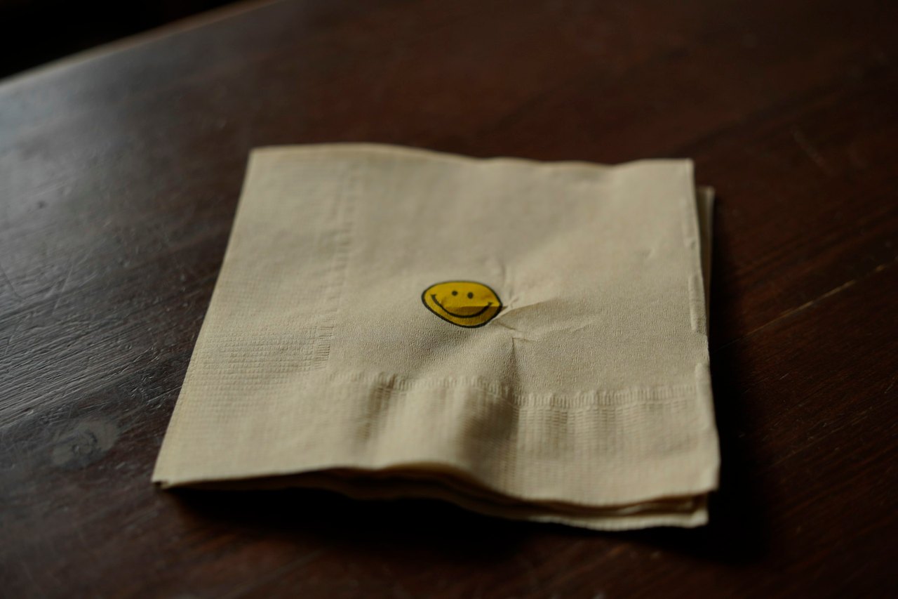 Eine zerknitterte Papierserviette mit einem kleinen gedruckten Smiley liegt auf einem dunklen Holztisch.