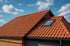 Rotes Ziegeldach mit Dachfenster und schwarzer Regenrinne unter blauem Himmel.