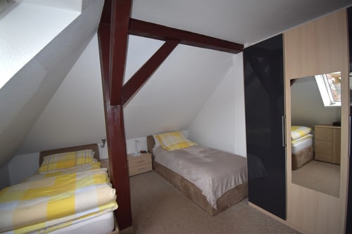 Schlafzimmer mit zwei Einzelbetten, Dachschrägen, Holzbalken und einem Kleiderschrank mit Spiegel.