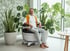 Eine lächelnde Frau sitzt in einem POWERCHAIR Sessel in einem Zimmer mit vielen Pflanzen.