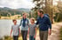 A family of four wearing hiking gear walks along a dirt path beside a mountain lake and evergreen forest.