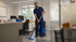 Ein Mann in blauer Uniform wischt einen Büroboden mit einem Mopp und Eimer.