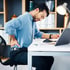 Man at desk holding lower back, indicating plantar fasciitis pain.