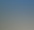 Ein weißes Haus mit rotbraunem Dach und einem verglasten Anbau, flankiert von zwei großen Bäumen, unter blauem Himmel.