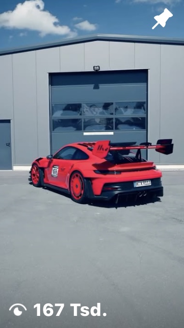 Roter Porsche 911 GT3 RS steht vor einer grauen Lagerhalle mit Rolltor unter blauem Himmel.
