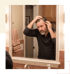 A middle-aged man with a beard looks in a bathroom mirror while touching his thinning hair and receding hairline.