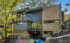 Modern multi-story house with dark gray siding, brick, large windows, surrounded by trees, and a stone patio.
