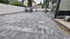 Modern gepflasterte Terrasse mit grau-nuancierten Steinplatten, weißem Sichtschutzzaun und einer dunklen Terrassenüberdachung.